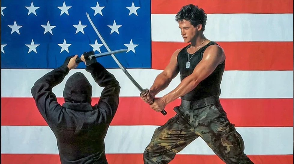 Michael Dudikoff fighting a black ninja in front of the American flag in American Ninja (1985).