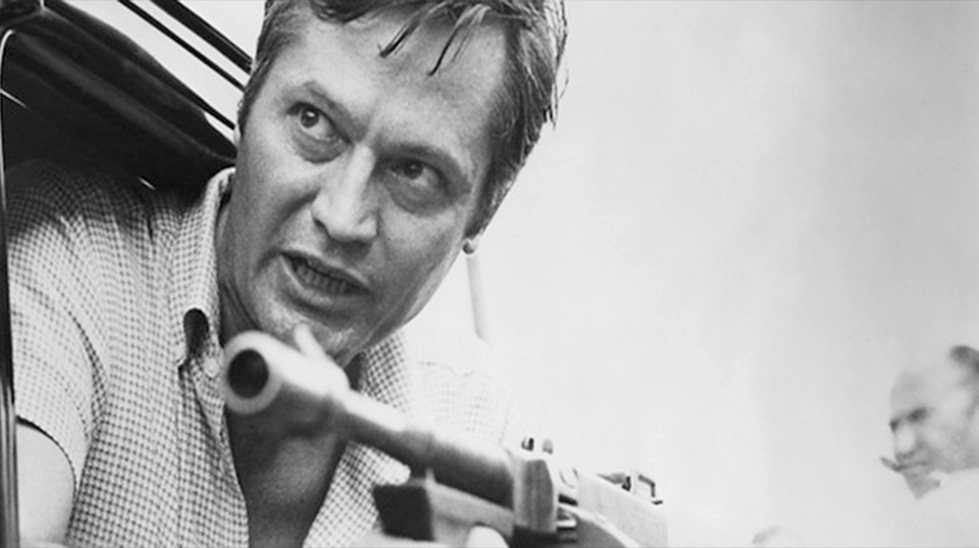 Siyah beyaz bir film setinde, elinde tüfekle hedefe odaklanmış, Amerikan bağımsız sinemasının öncüsü genç Roger Corman.