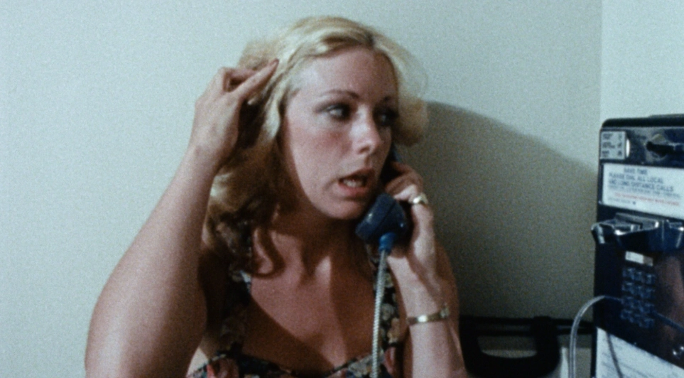 Delirium (1979) filminde sarışın baş kadın karakter, ankesörlü telefonla konuşurken endişeli bir ifadeyle saçına dokunuyor.